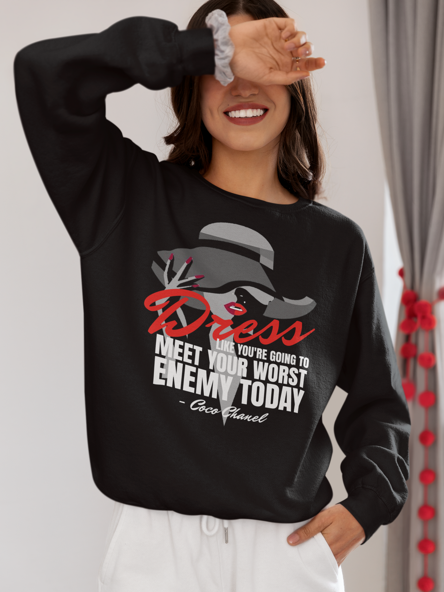 Woman wearing a black sweatshirt with a graphic design and text, smiling and posing.