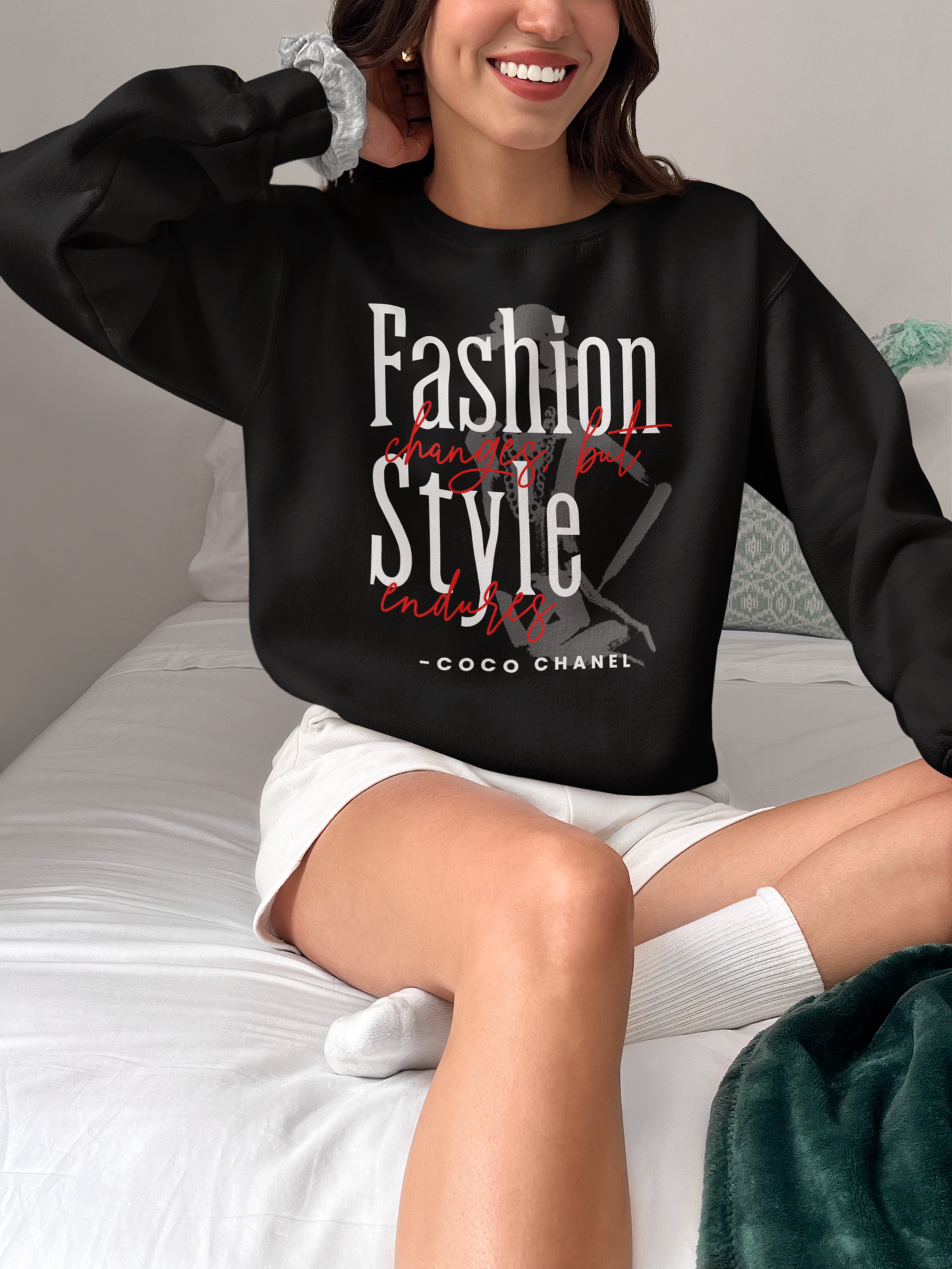 Person wearing a black sweatshirt with a fashion quote, sitting on a bed.